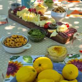 Outdoor table with lemons, cheese, fruits, and snacks arranged elegantly.