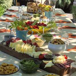 Outdoor table with charcuterie boards, cheeses, fruits, and breads.