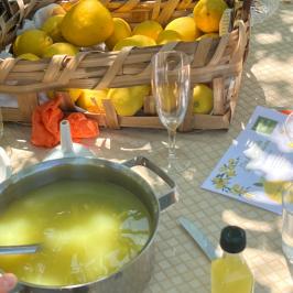 Table with lemons in a basket, pot of yellow liquid, and empty glassware.