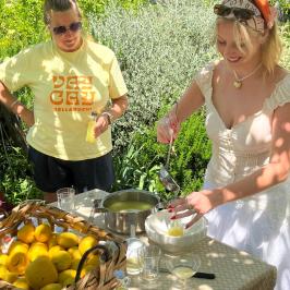 Two women making lemonade outdoors with fresh lemons and glasses on a table.
