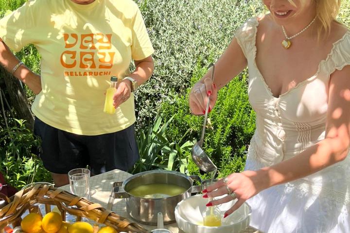 Two women making lemonade outdoors with fresh lemons and glasses on a table.