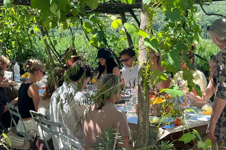 People dining outdoors under a grapevine canopy.
