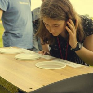 A person leaning over a table with covered dishes, outdoors in a field.