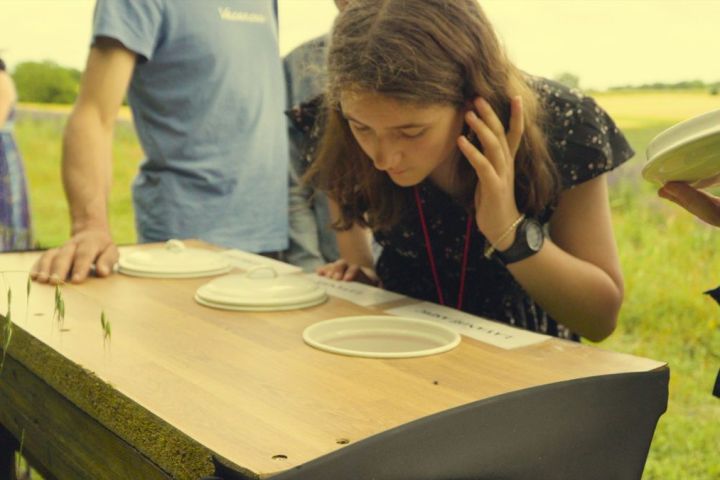 A person leaning over a table with covered dishes, outdoors in a field.