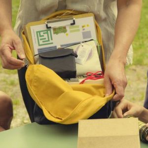 Person showing yellow backpack with papers and items inside on an outdoor table.