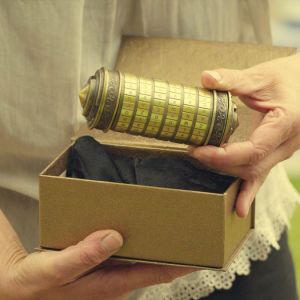Person holding a cylindrical puzzle box above an open cardboard box.
