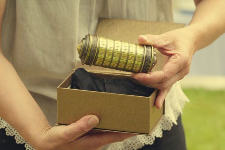 Person holding a cylindrical puzzle box above an open cardboard box.