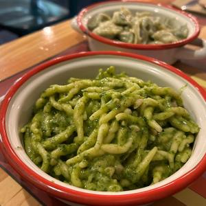 Close-up of pasta with green sauce in a red-rimmed bowl on a wooden table.