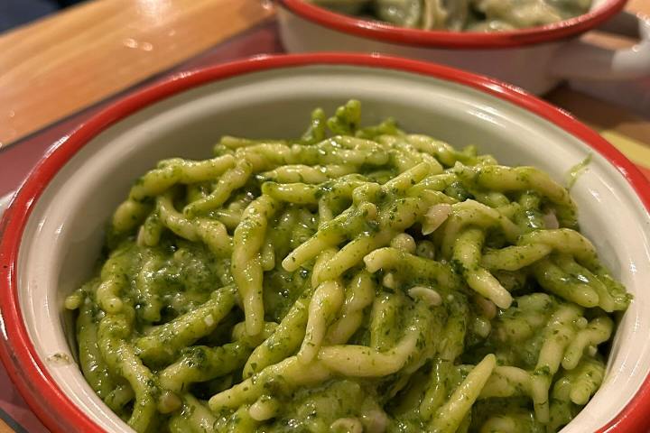 Close-up of pasta with green sauce in a red-rimmed bowl on a wooden table.