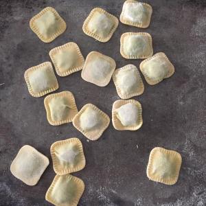 Uncooked square ravioli pieces scattered on a dark surface.