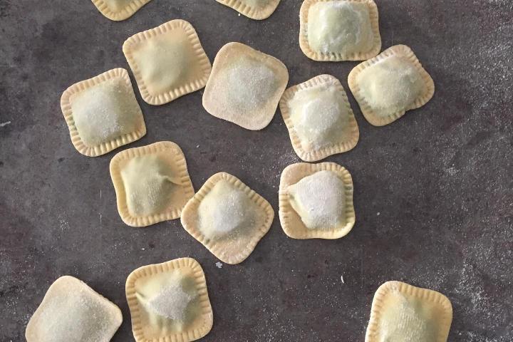 Uncooked square ravioli pieces scattered on a dark surface.