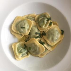 Plate of spinach ravioli garnished with herbs in a white bowl.