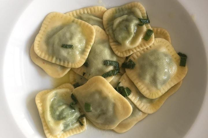 Plate of spinach ravioli garnished with herbs in a white bowl.