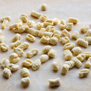 Uncooked gnocchi scattered on a floured surface.