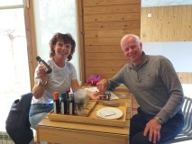 Two people smiling, holding bottles at a table with various oils.