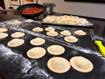 Homemade ravioli, fresh pasta, and a pan of tomato sauce on a floured kitchen counter.