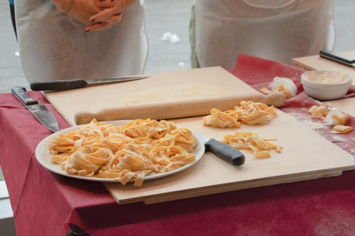 People in aprons making fresh pasta on a table with flour and knives.
