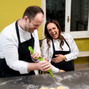 Two people in aprons laughing while cooking with dough on a floured surface.