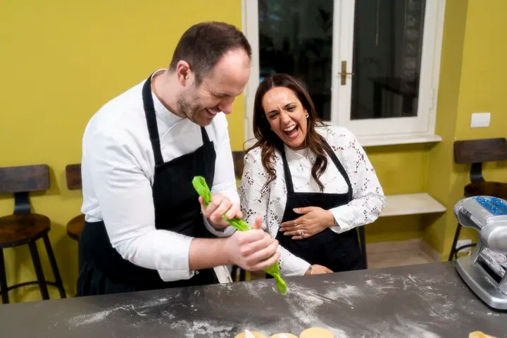 Two people in aprons laughing while cooking with dough on a floured surface.