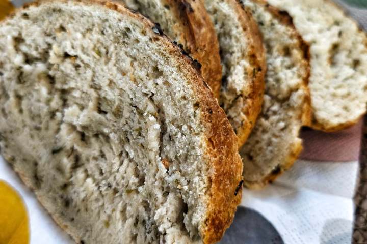 Sliced bread with herbs on a colorful napkin in a basket.