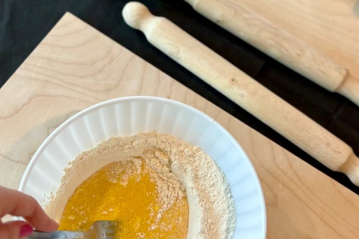 Hand mixing flour and eggs in a bowl on a wooden board with a fork.