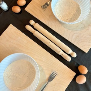 Two bowls of flour with forks on wooden boards, surrounded by eggs and rolling pins.