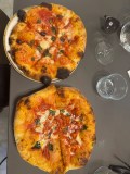 Two pizzas with tomato sauce and basil on a table with glasses and sunglasses.