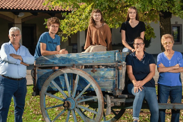 Six people posing around a blue wooden cart under a tree.