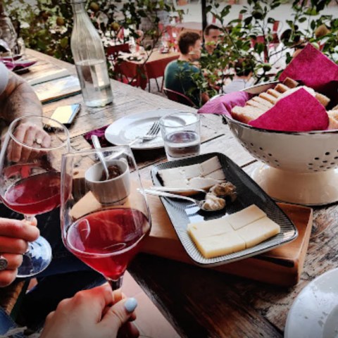 Two people holding wine glasses above a table with cheese and bread.