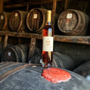 Wine bottle labeled Vin Santo on a wooden barrel in a dimly lit cellar.