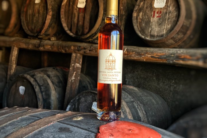 Wine bottle labeled Vin Santo on a wooden barrel in a dimly lit cellar.