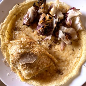 Plate with a crepe, grilled radicchio, cheese, and a slice of truffle on top.