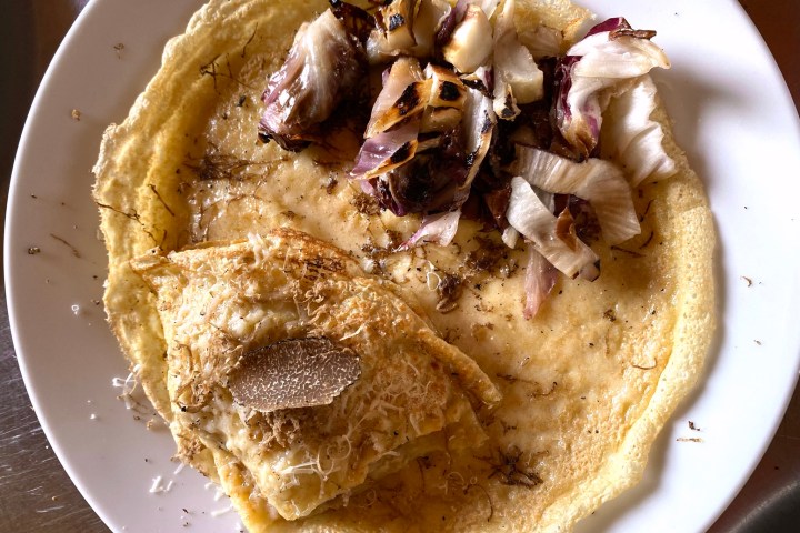 Plate with a crepe, grilled radicchio, cheese, and a slice of truffle on top.