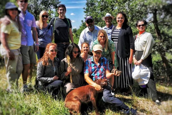 Group of people outdoors on grassy field with trees, some kneeling by large brown dog.