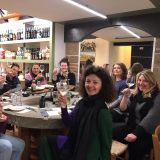 Group of people raising wine glasses around a table in a wine shop.
