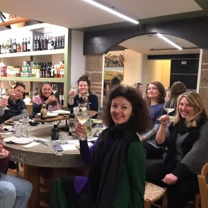 Group of people raising wine glasses around a table in a wine shop.