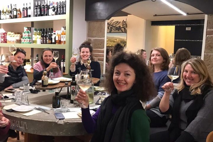 Group of people raising wine glasses around a table in a wine shop.
