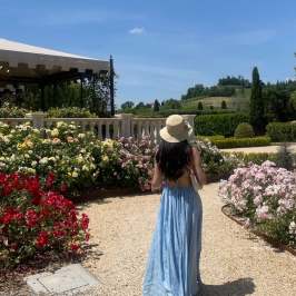 Woman in blue dress and hat walks in garden with roses.