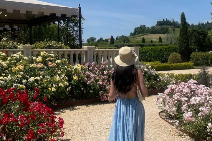 Woman in blue dress and hat walks in garden with roses.