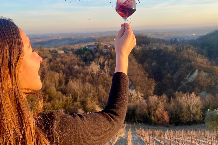 Woman holds wine glass spilling in vineyard, blue sky background.