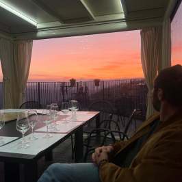 Man sitting by table with empty wine glasses, sunset view.
