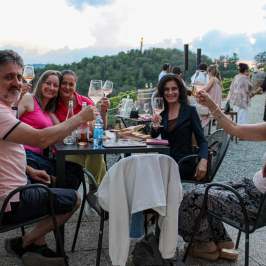 Group of people sitting at an outdoor table, holding wine glasses and smiling.