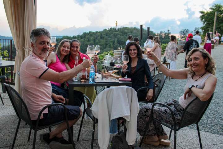 Group of people sitting at an outdoor table, holding wine glasses and smiling.