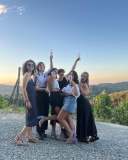 Group of six women celebrating outdoors at sunset with drinks.