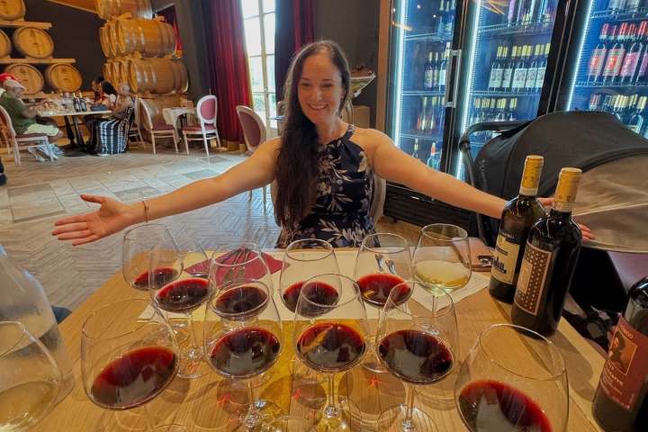 Smiling woman in a wine cellar with multiple glasses of red wine.