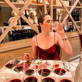 Woman tasting wine in a restaurant with wine glasses around her.