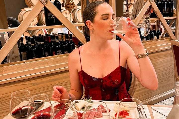 Woman tasting wine in a restaurant with wine glasses around her.