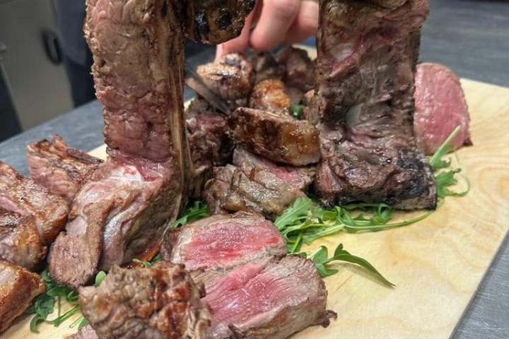 Cook slicing grilled steaks on a wooden board with arugula.