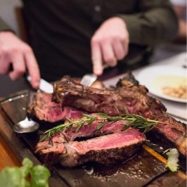 Person slicing juicy grilled steak garnished with rosemary on a wooden board.