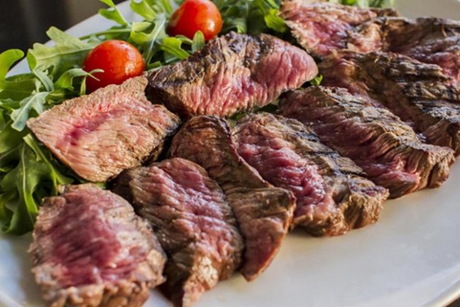 Sliced grilled steak with arugula and cherry tomatoes on a plate.